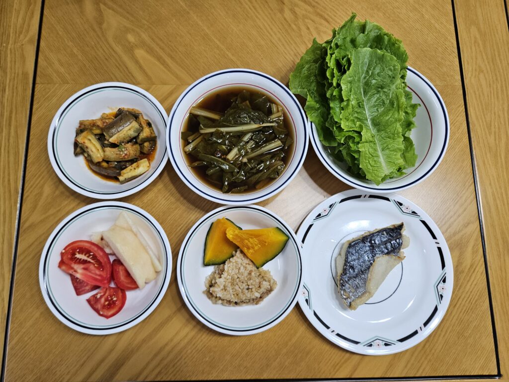 Meal with fish, brown rice, pumpkin, leafy greens, tomatoes, fruit, and vegetable side dishes